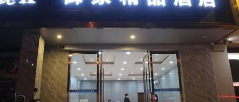 A hotel entrance with a reception desk, a man standing by the desk, and a sign above the entrance.