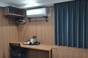 Habitación de hotel con un escritorio de madera, una silla, una cafetera, un teléfono y una botella de agua.
