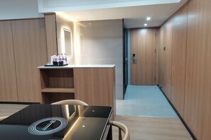 Quarto de hotel moderno com guarda-roupa de madeira, uma pequena mesa com um laptop e um espelho iluminado.