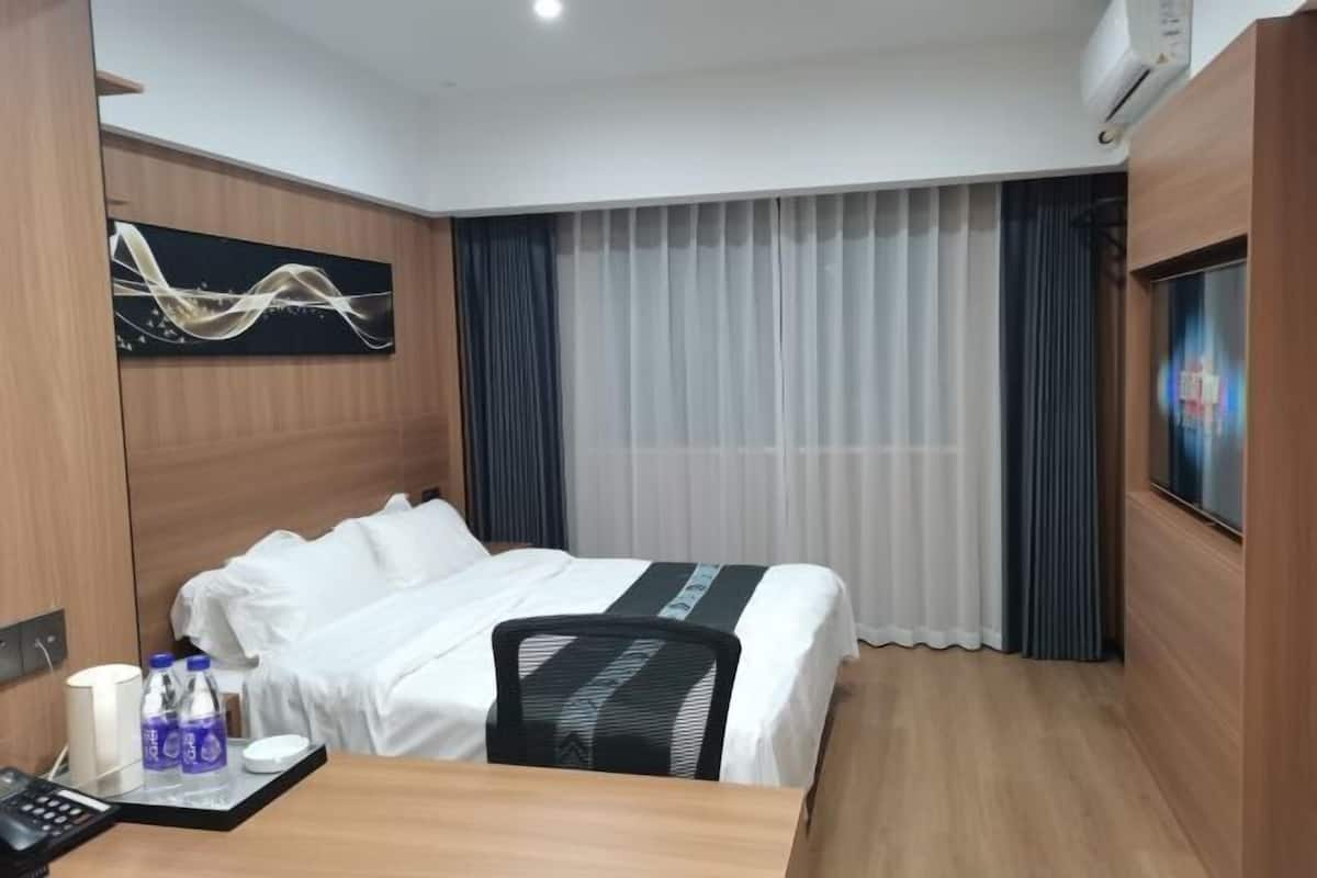 Habitación de hotel con cama, escritorio con silla, televisor y ventana con cortinas.