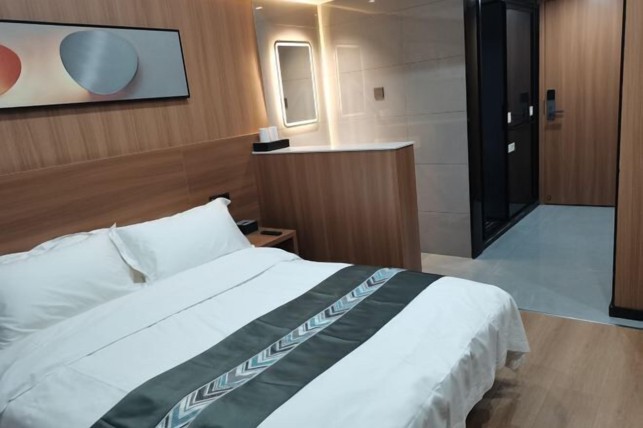 Une chambre d’hôtel comprenant un lit, une table de chevet, un miroir, une porte et une œuvre d’art accrochée au mur.