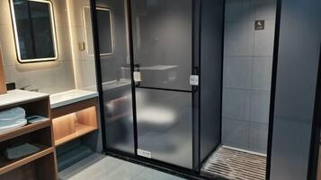 A modern bathroom with a glass shower enclosure, a vanity with a mirror, and a shelf with folded towels.
