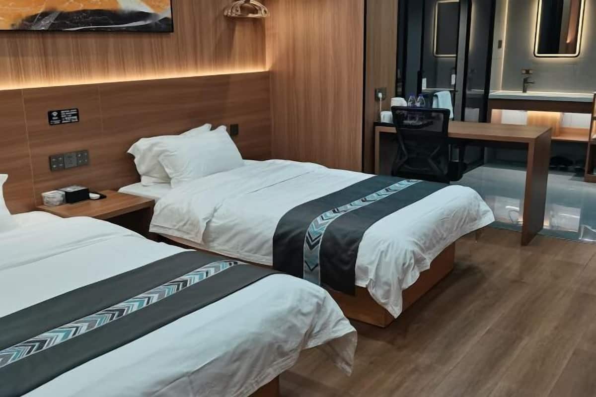 Habitación de hotel con dos camas, un escritorio, una silla, un espejo y una obra de arte colgada en la pared.