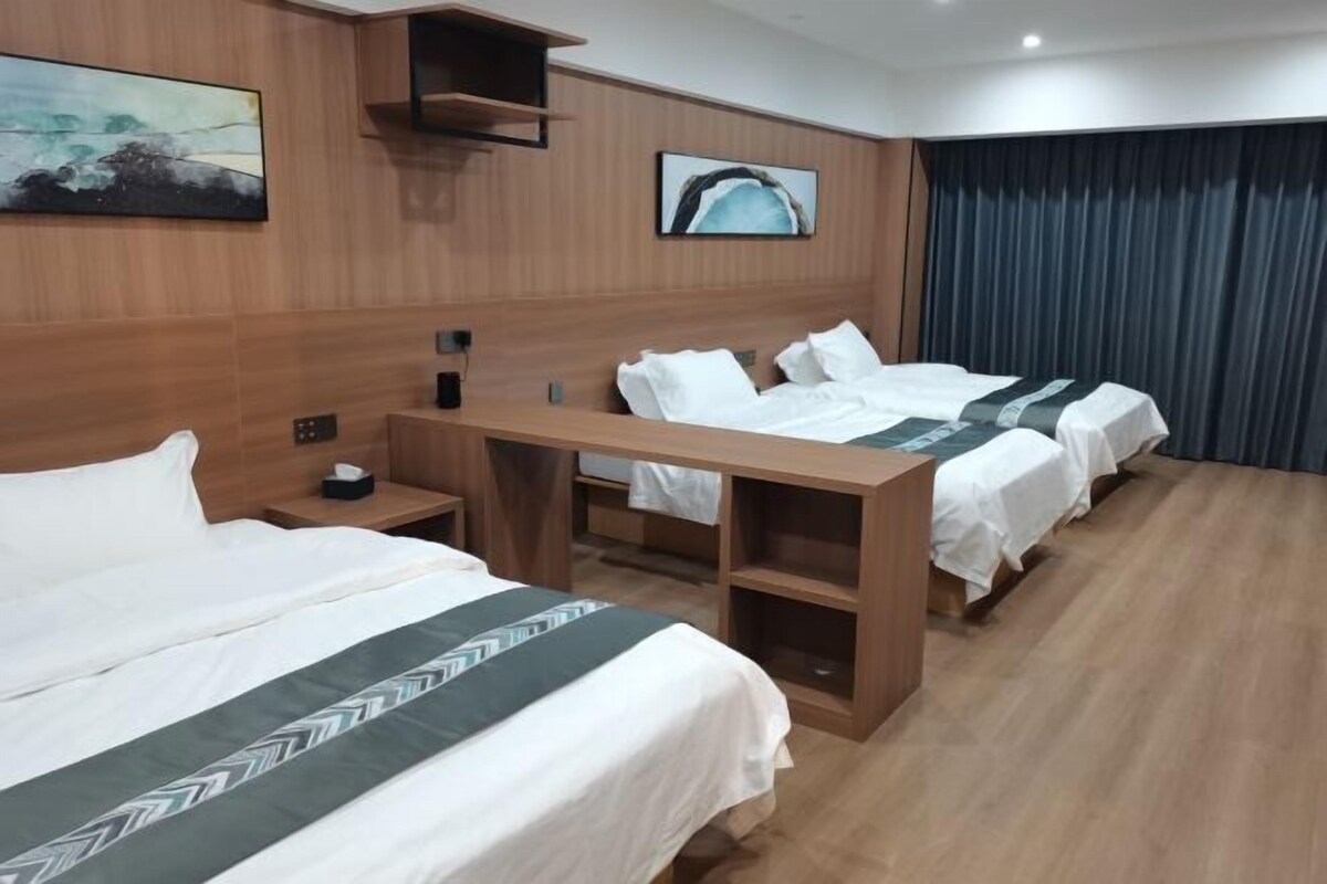 Quarto de hotel com três camas, lambris de madeira, uma escrivaninha e um quadro na parede.