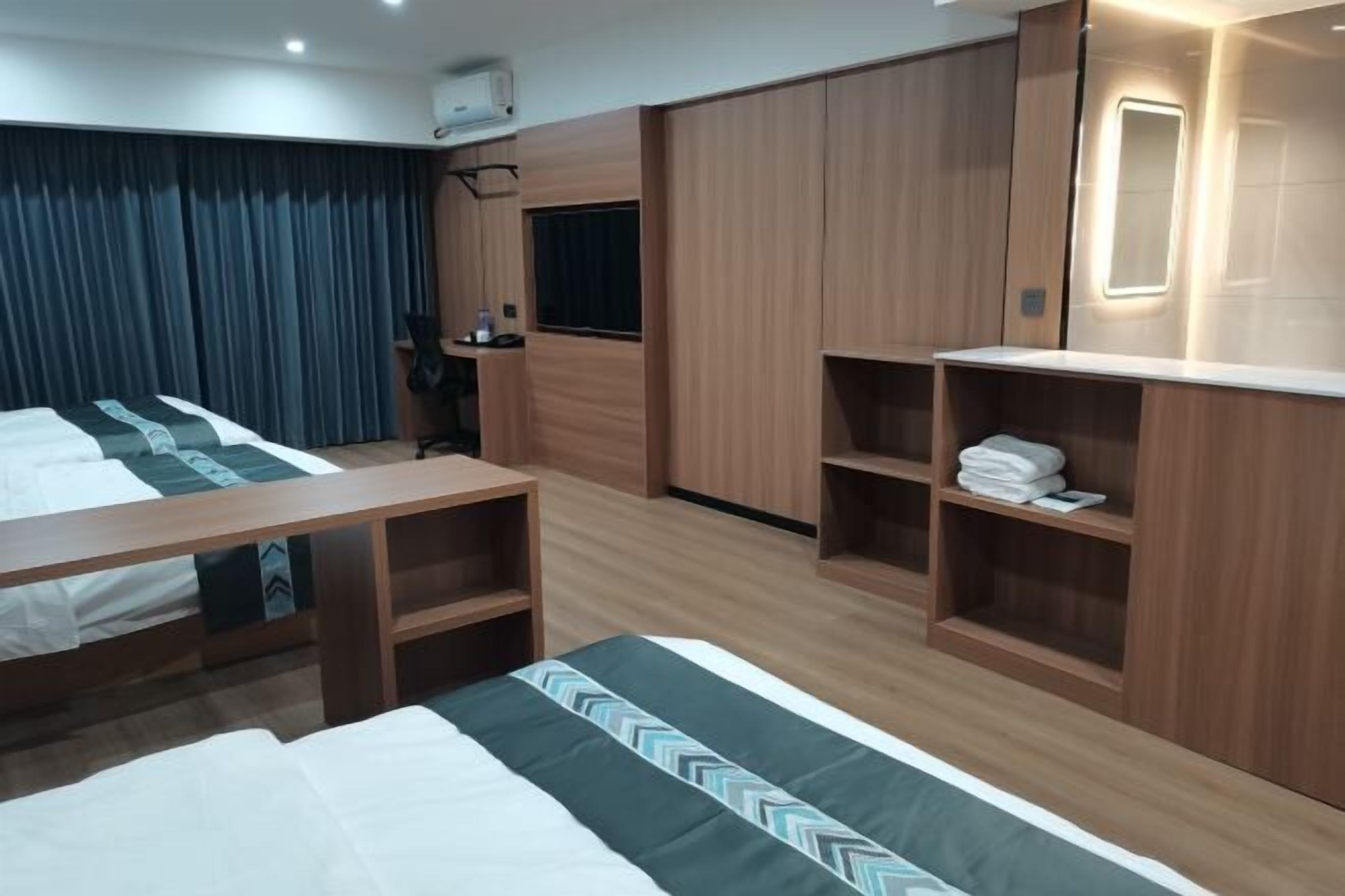 A hotel room with two beds, a desk, a wardrobe, and a mirror.