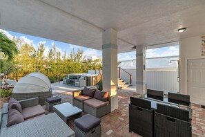 En udendørs terrasse med fletmøbler, et overdækket siddeområde og udsigt til træer og himlen.