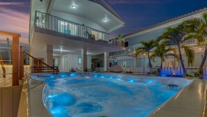 A hot tub with a wooden deck, a multi-level building with balconies, and palm trees. - Luxury 4B/3B, Private Canal, Kayaks, 13 ft Hot Tub, 4 H Mini-Golf & Pedal Boat. (Tavernier)