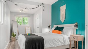 Un dormitorio con cama, mesita de noche, un adorno de macramé en la pared y una ventana con vista a la vegetación.