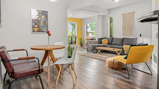 Una sala de estar moderna con un sofá, una mesa de centro y sillas. Hay una mesa de comedor con sillas y un jarrón de flores.
