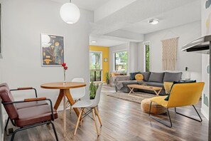 A modern living room with a sofa, coffee table, and chairs. There is a dining table with chairs and a vase of flowers.