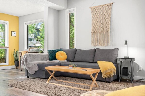 A modern living room with a grey sofa, wooden coffee table, and a macrame wall hanging.
