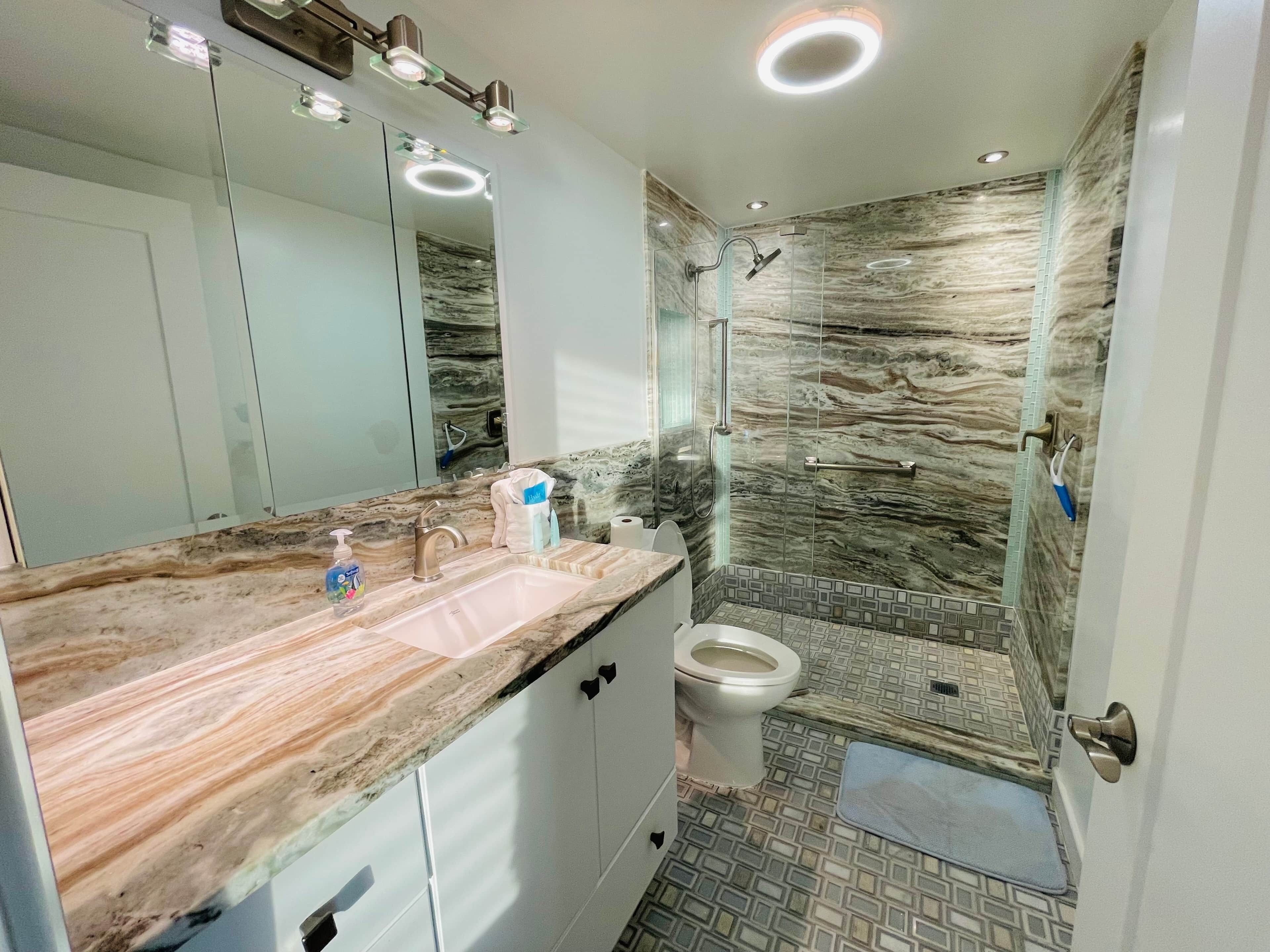 Un baño moderno con encimera de mármol, cabina de ducha de vidrio y un inodoro.