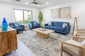 A modern living room with a blue sofa set, a wooden coffee table, and a large window providing a view of the outdoors.