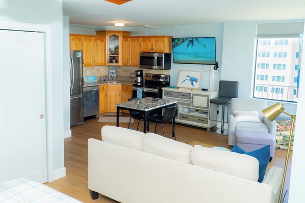 A compact living space with a kitchenette, a white sofa, a dining table, and a view of the city through a window.