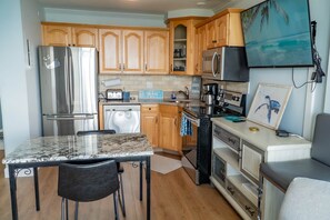 A kitchen with wooden cabinets, a stainless steel refrigerator, a microwave, a coffee maker, and a TV mounted on the wall.