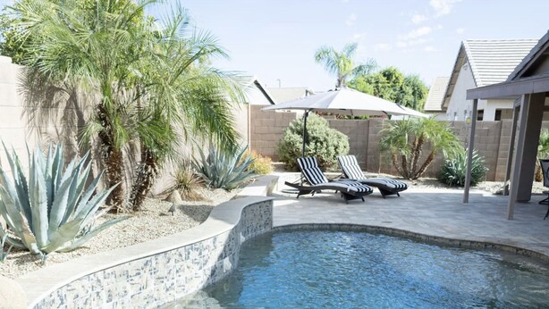 A swimming pool with lounge chairs and an umbrella, surrounded by various plants and a brick wall. - The Gilbert Haven - comfortable, stylish w/ pool (Gilbert)