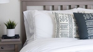 A neatly made bed with white bedding, a patterned pillow, and a small potted plant on a bedside table. - The Gilbert Haven - comfortable, stylish w/ pool (Gilbert)