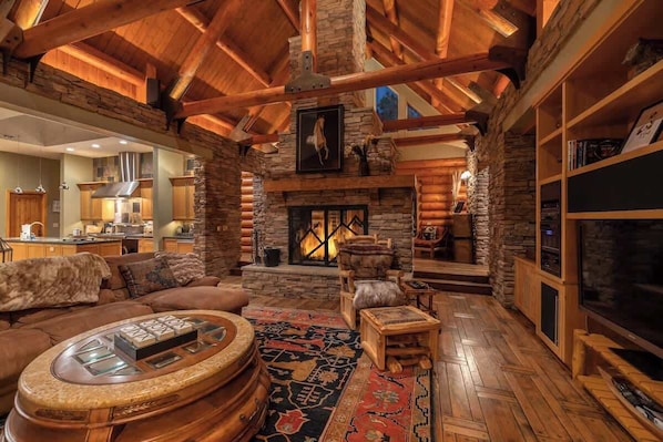 A log cabin interior with a stone fireplace, wooden furniture, and a television.