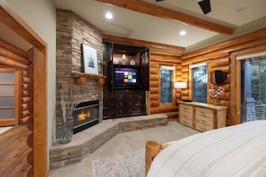 A log cabin interior with a stone fireplace, wooden walls, a television, and a bed.