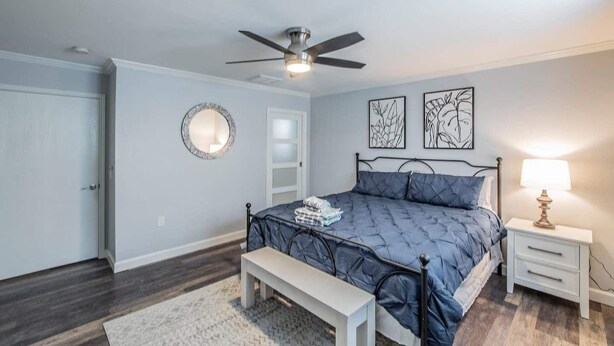 Um quarto com uma cama, um ventilador de teto, uma mesa de cabeceira com abajur e um espelho na parede.