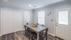 Uma área de refeições com mesa e cadeiras de madeira, portas brancas e uma janela com persianas.