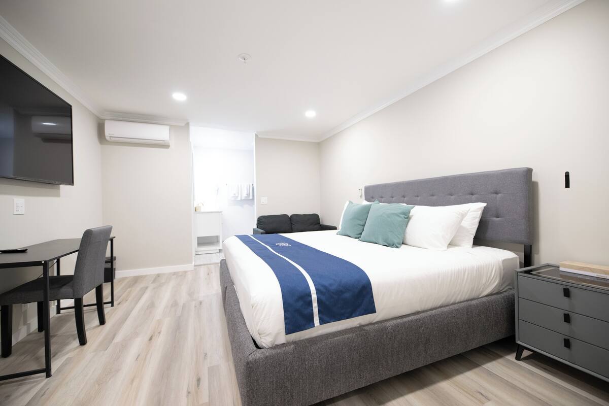 A modern bedroom with a large bed, bedside tables, a desk, and a flat-screen TV.