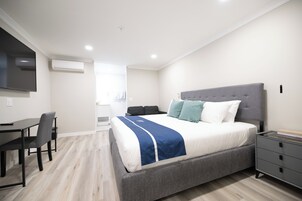 Quarto moderno com uma cama grande, mesas de cabeceira, escrivaninha e televisão de tela plana.