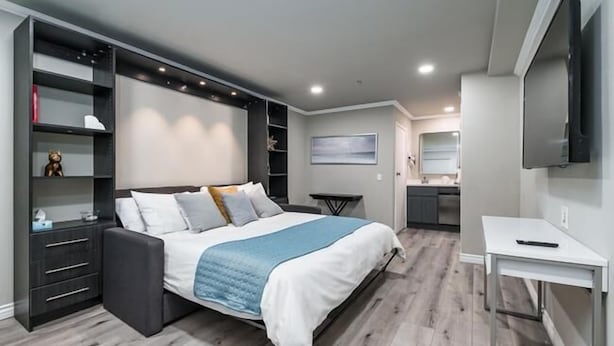 Un dormitorio moderno con una cama grande, estanterías empotradas, un escritorio pequeño y un televisor.