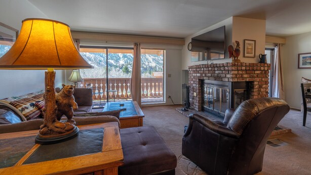 A living room with a fireplace, a bear sculpture, a lamp, and a view of mountains through the window. - Interlaken #19 - 3 Bedroom 3 Bathroom Unit (June Lake)
