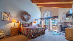 A bedroom with a bed, two bedside lamps, a wooden dresser, a fireplace, and a view of the outdoors. - Interlaken #19 - 3 Bedroom 3 Bathroom Unit (June Lake)