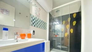 A modern bathroom with a white sink, blue countertop, and a glass shower enclosure with leaf decals. - Check-in 24horas madrid (Madrid)