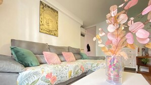 A modern living room with a grey sofa, floral bedding, a Buddha painting, and a vase with dried flowers. - Check-in 24horas madrid (Madrid)