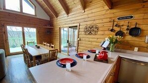 A wooden cabin interior with a dining area, kitchen, and a sliding glass door leading to a deck.