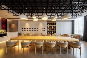 Uma sala de jantar moderna com uma mesa comprida e várias cadeiras, uma estante de livros e iluminação pendente.