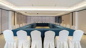 A conference room with a long table, white chairs, and a modern ceiling design.