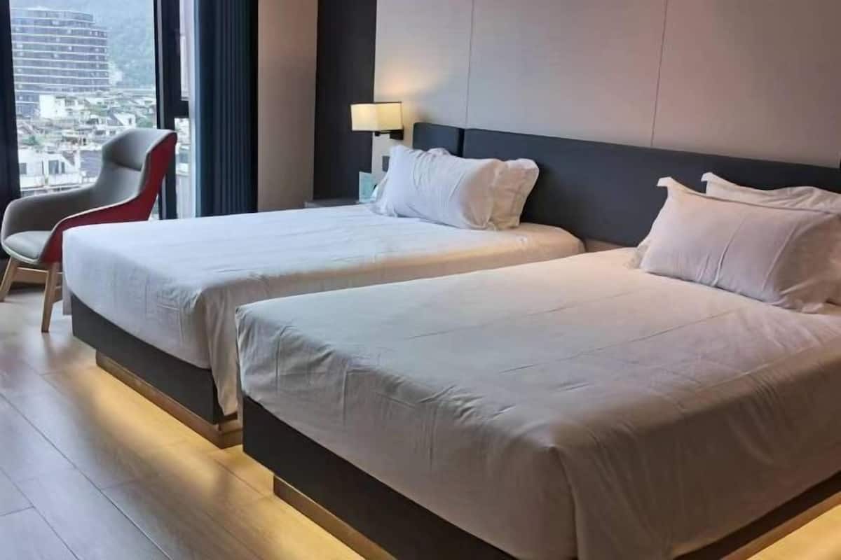Hotellihuone, jossa on kaksi sänkyä, tuoli, yöpöytä ja näkymä kaupunkiin.