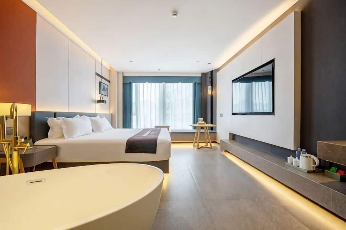 Moderni hotellihuone, jossa on suuri sänky, erillinen oleskelualue, suuri kylpyamme ja suuri ikkuna, jossa on verhot.