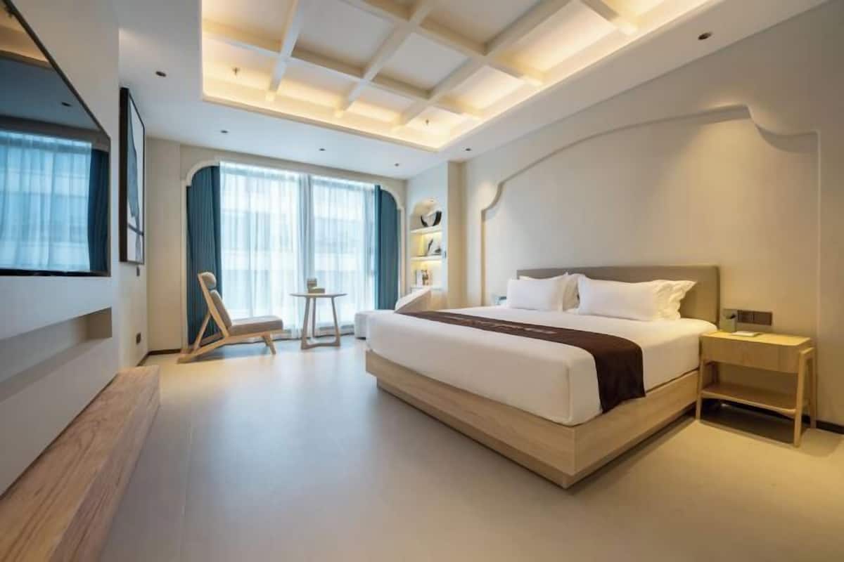 Moderni hotellihuone, jossa on suuri sänky, pieni sivupöytä, tuoli ja työp öytä.