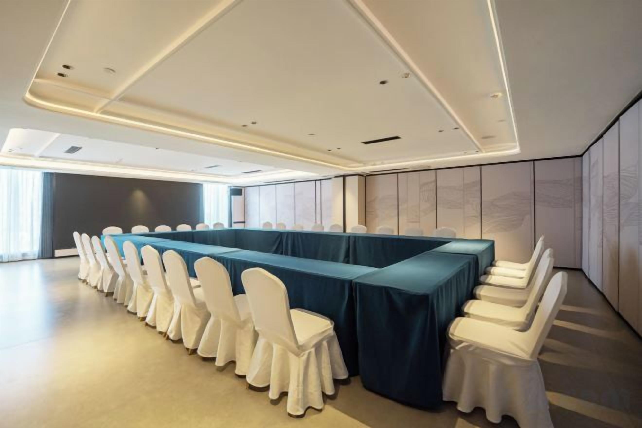 A conference room with a long table, white chairs, and a blue tablecloth.