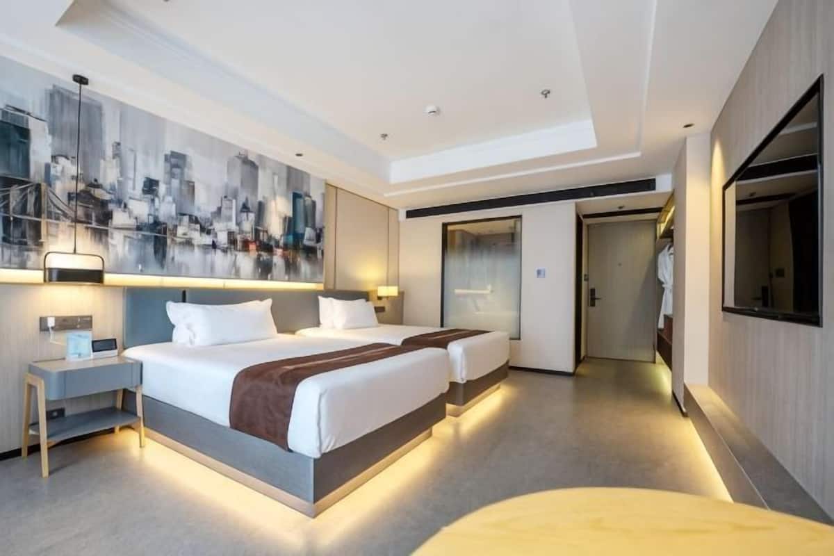 Moderni hotellihuone, jossa on suuri sänky, yöpöydät, taulu seinällä ja peili.