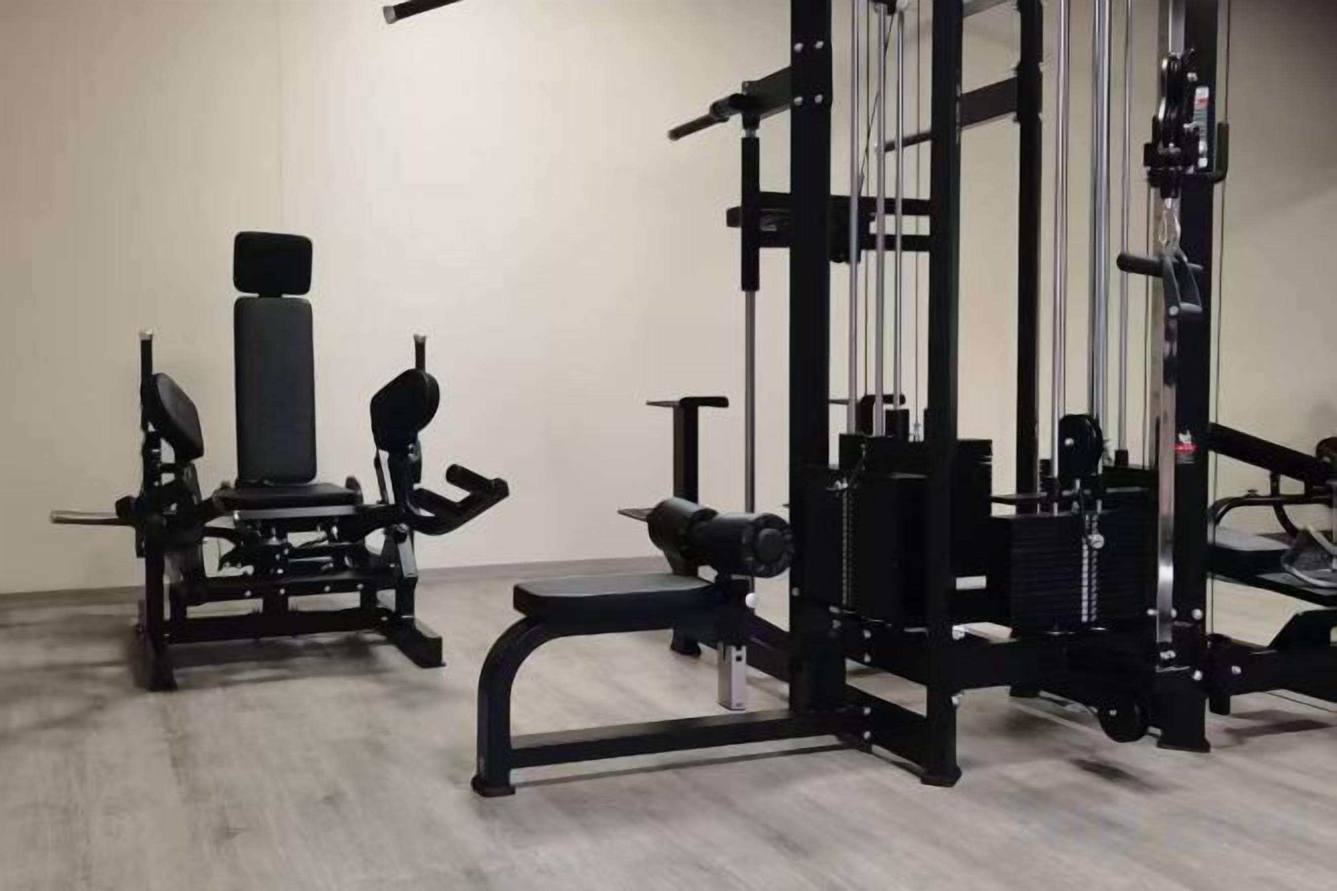 A gym with various exercise equipment, including a bench press, squat rack, and weight benches.