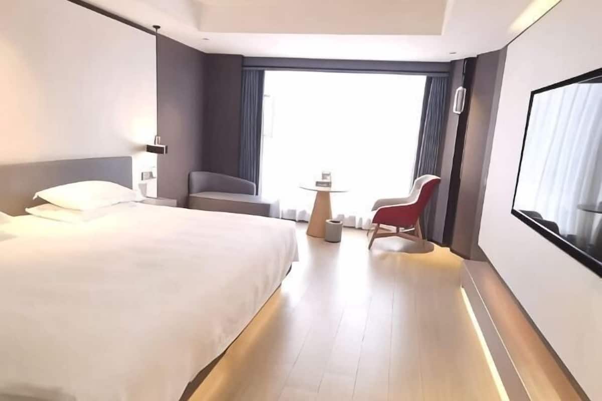 Hotellihuone, jossa on suuri sänky, pieni pöytä, punainen tuoli ja suuri ikkuna.