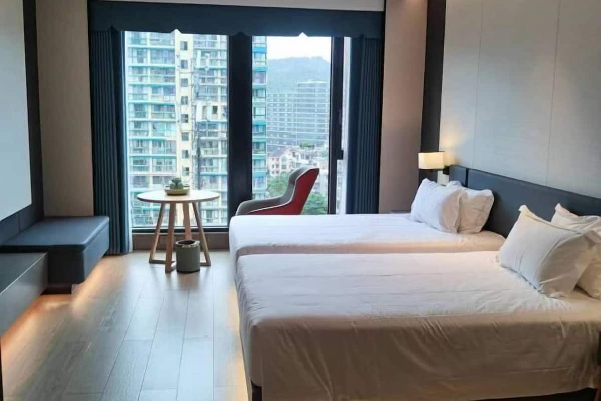 Hotellihuone, jossa on suuri ikkuna, kaksi sänkyä, pieni pöytä ja tuoli.