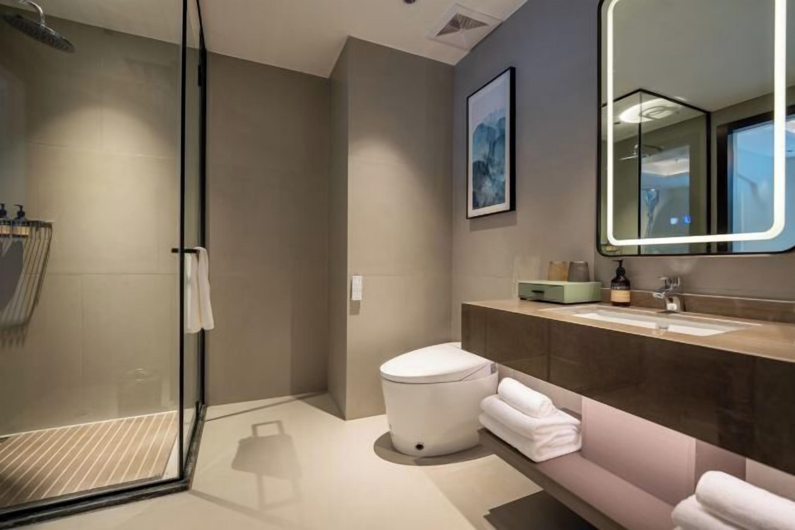 Un baño moderno con cabina de ducha de vidrio, inodoro blanco, tocador con espejo y toallas dobladas con cuidado.