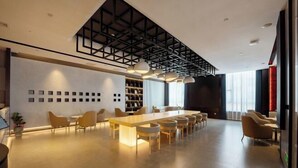 Un moderno vestíbulo de hotel con un mostrador de recepción de madera alargado, asientos cómodos y un techo alto con vigas a la vista.