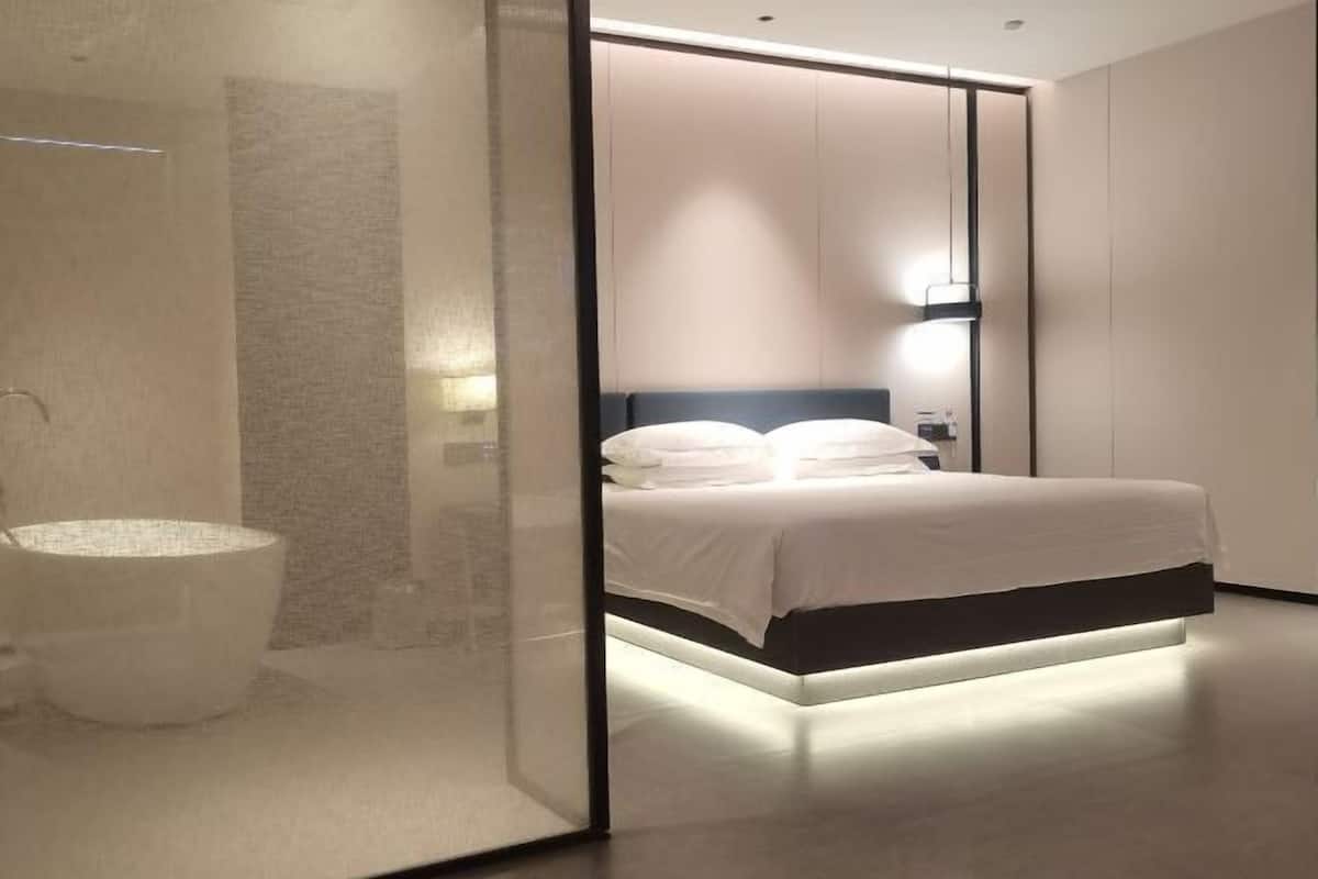 Moderni hotellihuone, jossa on suuri sänky, yöpöytä ja lasinen sermi.