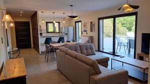 A modern living room with a sectional sofa, a dining area with chairs, a kitchen with a counter, and a large sliding glass door to an outdoor area. - Porto Vecchio villa with heated pool near San Ciprianu beach (Porto Vecchio)
