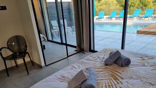A hotel room with a bed, a chair, and a view of a pool with lounge chairs. - Porto Vecchio villa with heated pool near San Ciprianu beach (Porto Vecchio)