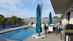 A swimming pool with lounge chairs and umbrellas, a barbecue area, and a view of trees. - Porto Vecchio villa with heated pool near San Ciprianu beach (Porto Vecchio)