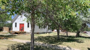 A white house with a red door, surrounded by trees and a grassy yard. - 4 bedrooms 3 bath, Tranquil Home, Master suite & Jet tub, Mins from Hot Springs (Thermopolis)